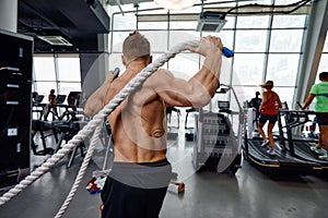 Muscular powerful aggressive man training with rope in functional training fitness gym. Motion blur