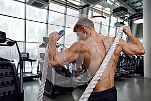 Muscular powerful aggressive man training with rope in functional training fitness gym. Motion blur