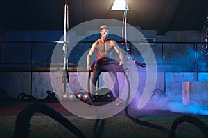 Muscular powerful man training with rope in functional training gym