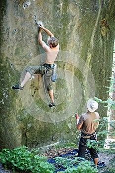 Muscular rock climber climbs on cliff wall with rope