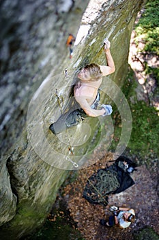 Muscular rock climber climbs on cliff wall with rope