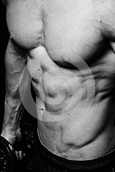 Muscular torso of young sporty man with perfect abs close up. Black and white isolated on black background