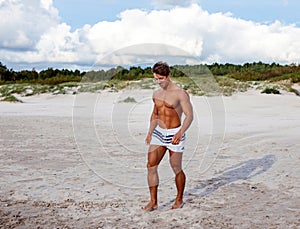 Muscular shirtless guy walking on a beach.