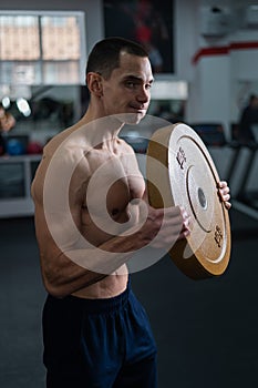 Muscular shirtless man doing exercise with weight plate in gym.