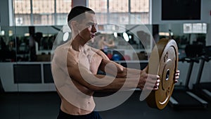 Muscular shirtless man doing exercise with weight plate in gym.