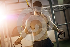 Muscular shirtless man training with fitness straps at gym