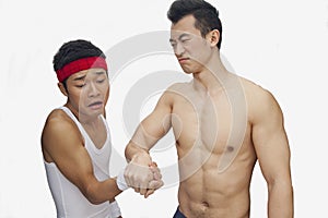 Muscular shirtless young man beating another young man at arm wrestling, studio shot