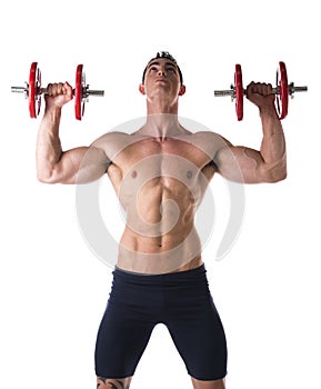 Muscular shirtless young man exercising shoulders with dumbbells