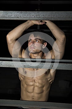 Muscular shirtless young man resting against metal structure
