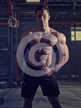 Muscular, shirtless young man resting in gym during workout