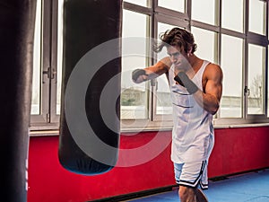 Muscular sportive man training with punching bag while boxing