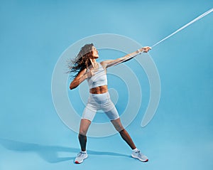 Muscular sportswoman exercising with resistance band on blue background. Female working out with elastic band