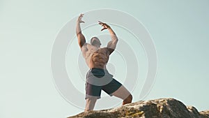 Muscular strong black bodybuilder posing on the rock against blue cloudy sky. Perfection of human's body