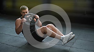 Muscular strong man doing russian twist exercise with weight from barbell.