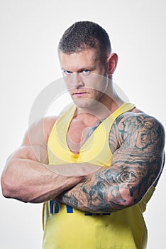 Muscular strong shredded man with blue eyes and tattoo in the yellow tank top the white background