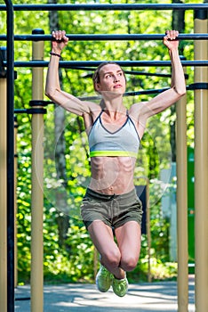 Muscular strong woman on the crossbar is engaged in the park