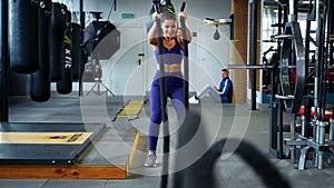 Muscular woman doing battle rope exercise in cross training gym.