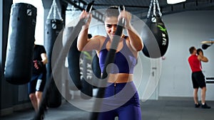 Muscular woman doing battle rope exercise in cross training gym.