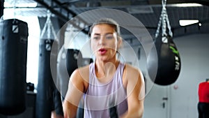 Muscular woman doing battle rope exercise in cross training gym.