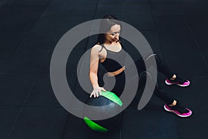 Muscular woman doing intense core workout in gym. Strong female doing core exercise on fitness mat with medicine ball in