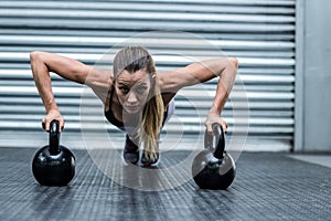 Muscular woman doing pushups with kettlebells