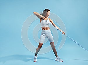 Muscular woman exercising with elastic band. Female in fitnesswear pulling resistance band on blue background