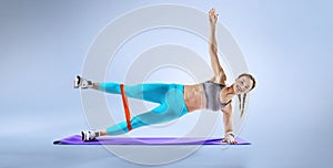 Muscular woman on a plank position use fitness gum. Muscular and strong girl exercising.