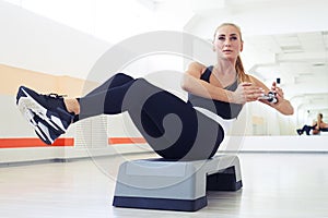 Muscular woman with slim fitness body doing exercises with dumbbell on step platform