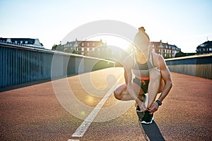 Muscular woman ties her running shoes on bridge