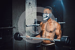 Muscular young african american man in mask lifting barbell on biceps. Exercise for biceps with barbell. black man in gym