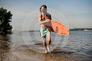 Muscular beach lifeguard running along the river bank with life-saving equipment