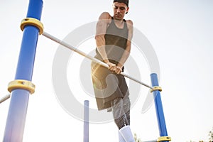 Muscular young Caucasian male doing pull ups exercises on crossbar outdoors. Athletic runner training hard at sunny afternoon