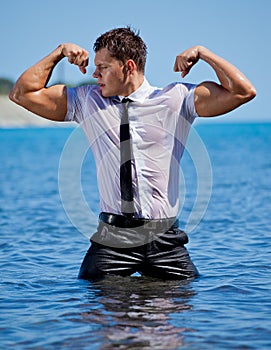 Muscular young guy standing in the sea in business suit