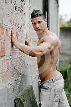 Muscular young latino man shirtless in jeans leaning against wall