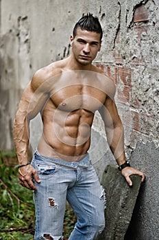 Muscular young latino man shirtless in jeans leaning on wall