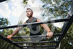 Muscular young male exercising core on horizontal bars