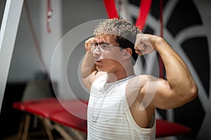 Muscular young man checking his biceps muscles training at gym, confident bodybuilder working out with weights in sport