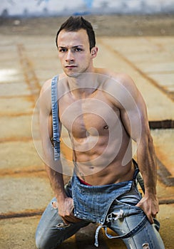 Muscular young man with denim overalls kneeling