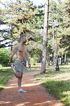 Muscular young man doing stretching exercises in the park