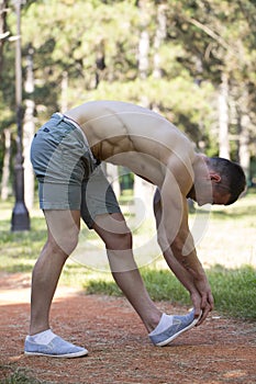 The muscular young man doing stretching exercises in the park