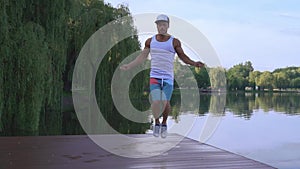 Muscular young man jumping with skipping rope near lake