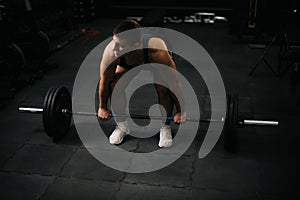 Muscular young man with perfect beautiful body wearing sportswear lifting heavy barbell from floor