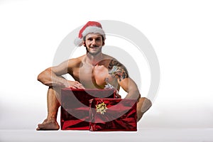 Muscular young man in Santa Claus hat with Christmas gift