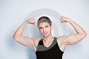 Muscular young man shows biceps in black t-shirt on a white background. Copy, empty space for text