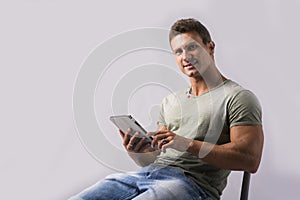 Muscular young man sitting on chair reading from ebook device