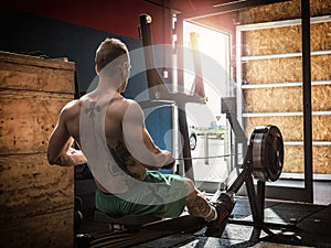 Muscular young man, training back on rowing machine