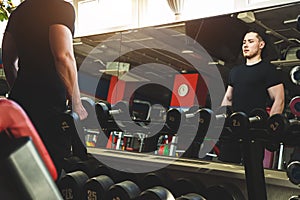 Muscular young man is training in the gym in front of the mirror