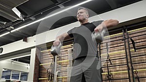 Muscular young man training with kettlebells in modern gym.