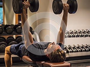 Muscular young man, training pecs on gym bench