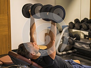 Muscular young man, training pecs on gym bench